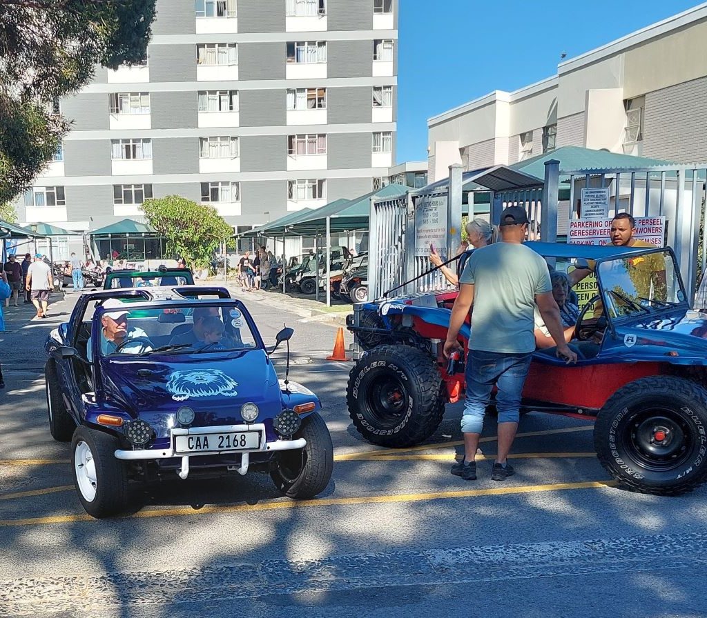 Mario taking a senior resident for a drive in his custom beach buggy at the Wild Buggers Beach Buggy Club Huis Uitsig event.