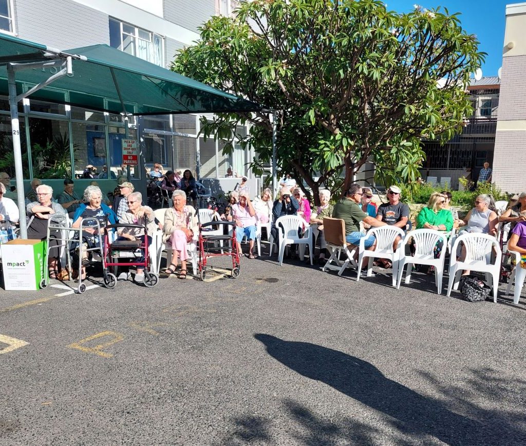 Seniors at Huis Uitsig sitting in the sun and enjoying the lively atmosphere of the Wild Buggers Beach Buggy Club visit.