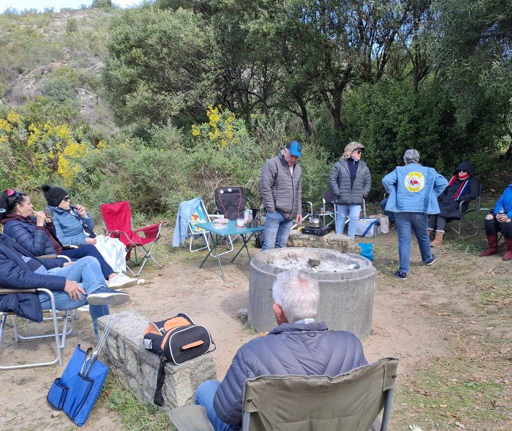 Wild Buggers Beach Buggy Club members chatting around a fire that has died down during a club event.