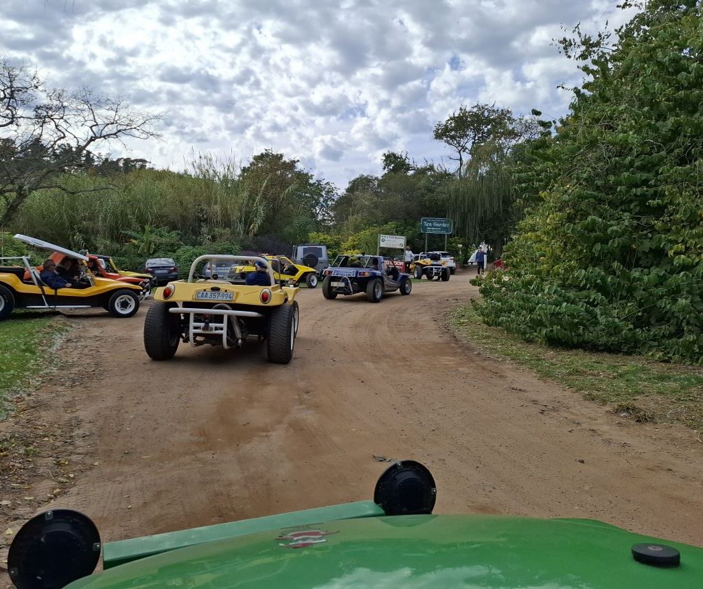 A line of Wild Buggers beach buggies navigating and parking in a designated parking area at Helderberg Farm, the milkshake stop, with other vehicles and potentially some open grounds or features of the establishment visible in the background, during Wiehann's Run.