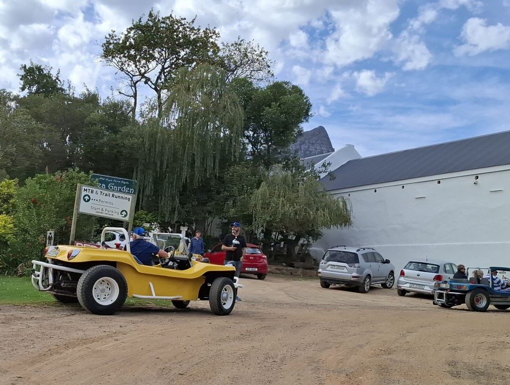 Wild Buggers beach buggies are seen navigating and parking in the designated area at Helderberg Farm, the milkshake stop, with a visible farm building and other vehicles in the background during Wiehann's Run.