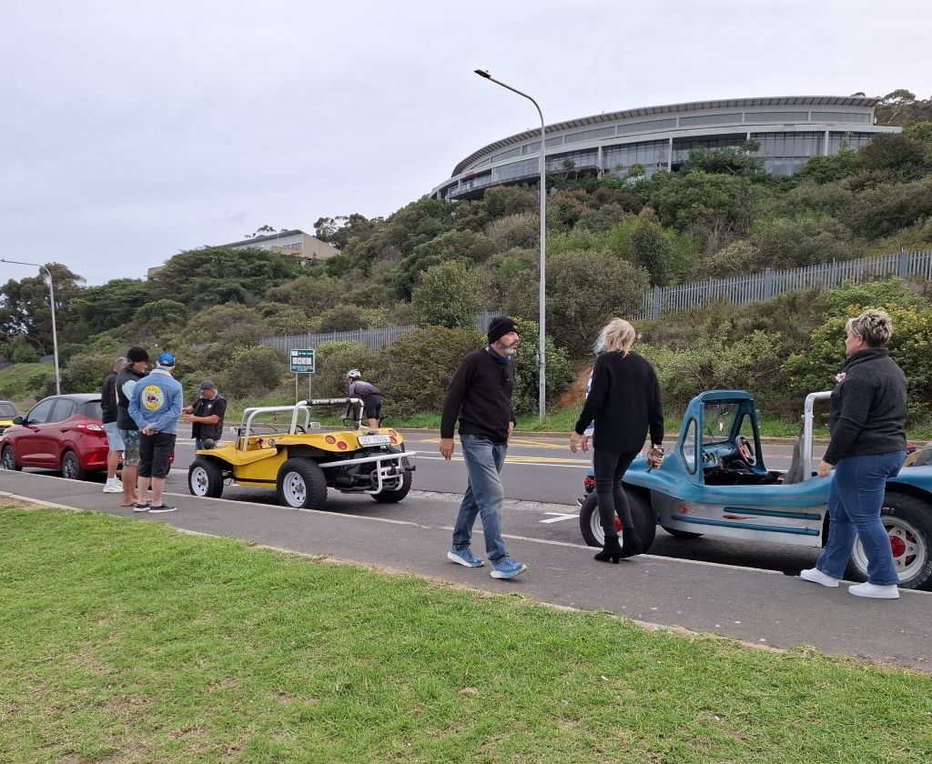 A line of diverse classic beach buggies and air-cooled VWs, including a VW Beetle, gathered at the Uys Krige Lookout point, with Table Mountain or a scenic Cape Town backdrop, ready for Wiehann's Run.