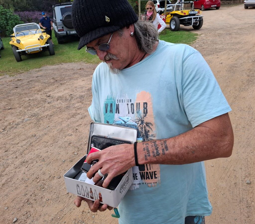 Tony is seen standing in the parking area at Helderberg Farm during Wiehann's Run, carefully preparing his medication with concentration, as other beach buggies and club members are visible in the background.