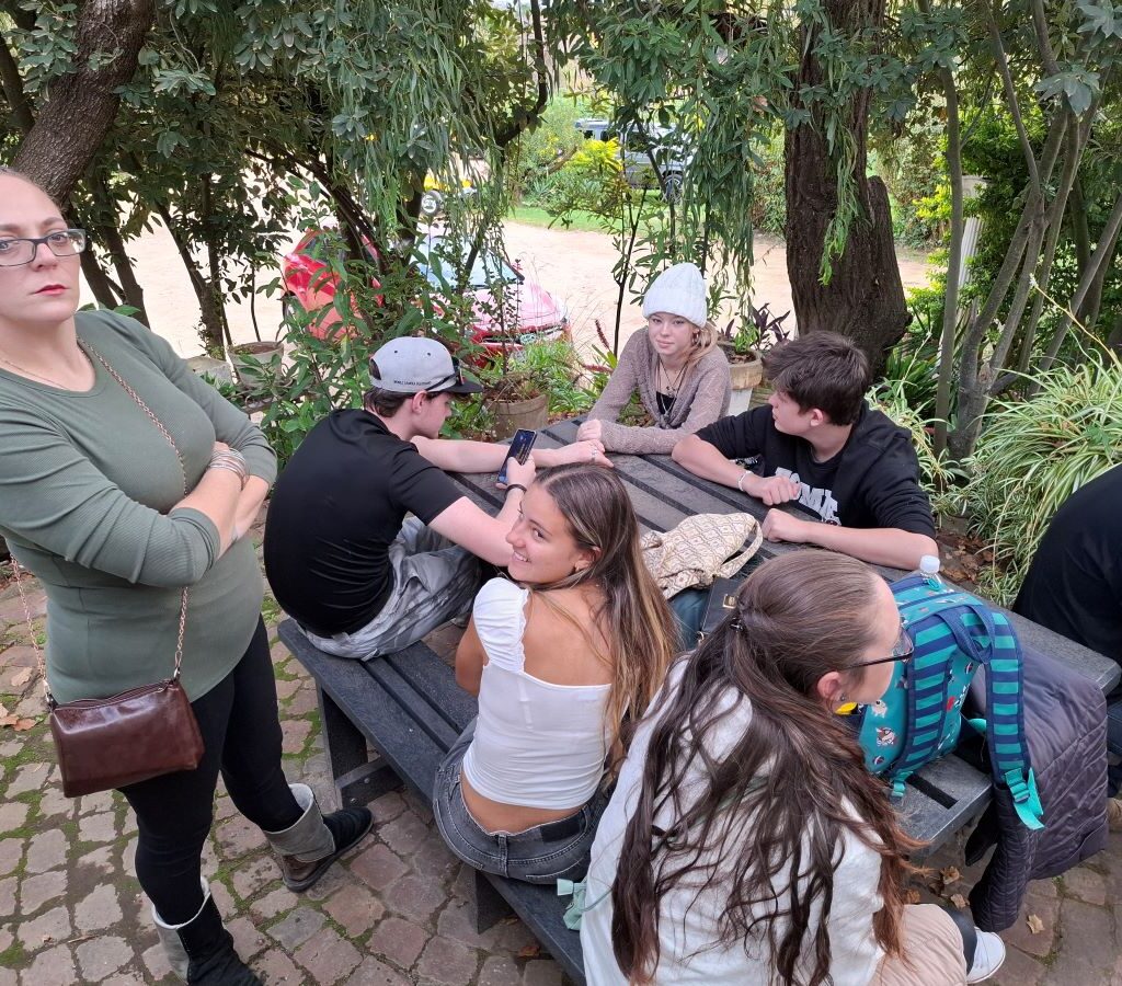 A group of Wild Buggers Beach Buggy Club members, all wearing black as a tribute, are seen sitting and standing in a relaxed manner in the garden area of Helderberg Farm, with empty hands still waiting for their milkshakes during Wiehann's Run.