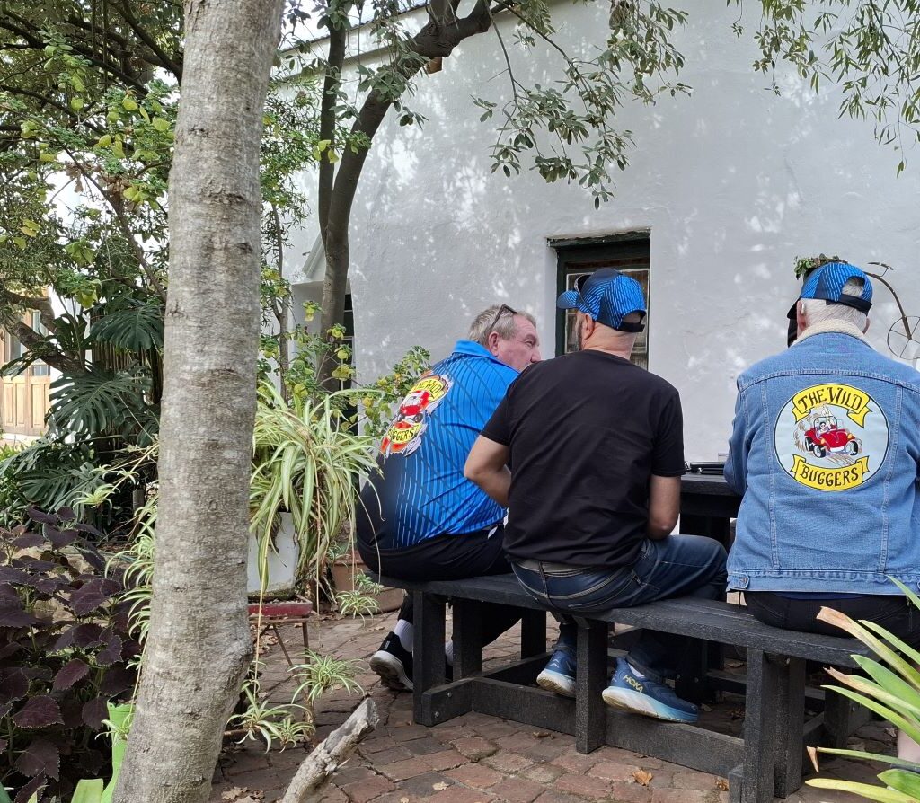 Chris, Wiehann, and Jacques from the Wild Buggers Beach Buggy Club are seen waiting for their milkshakes at Helderberg Farm, showcasing their anticipation and camaraderie during Wiehann's Run.