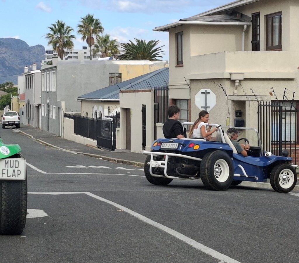 A blue Beamish beach buggy, driven by Craig, is seen rounding a corner on a scenic road during a Wild Buggers run.