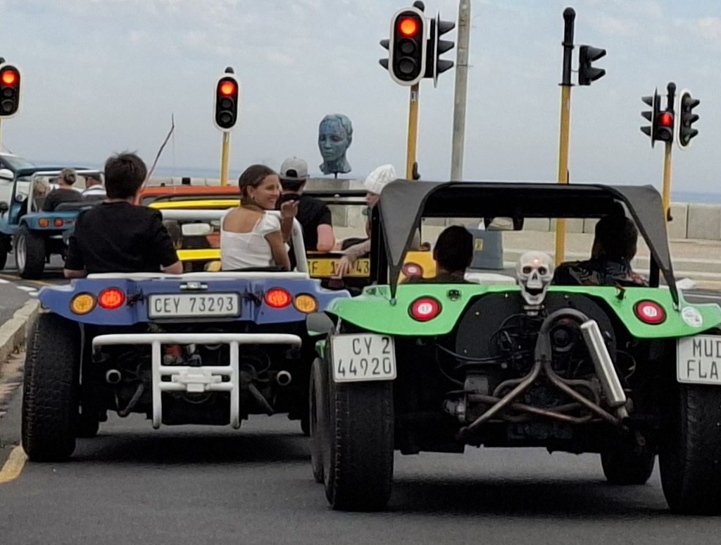 A convoy of Wild Buggers beach buggies is seen making a left turn at a traffic light, heading towards the Strand area, under a clear sky during Wiehann's Run.