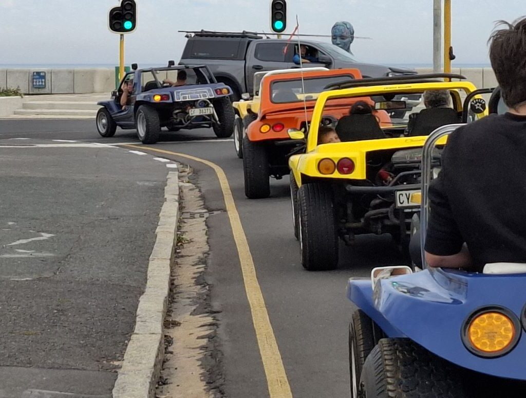A line of Wild Buggers beach buggies making another left turn on a road, indicating their continued journey through urban or suburban areas towards their next destination during Wiehann's Run.
