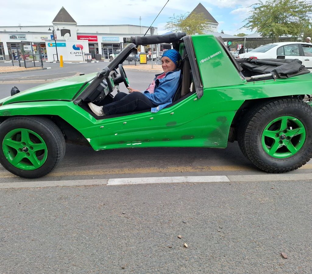 Mickey is seated in Anton Kleyn's vibrant green Kango beach buggy, which features a 1400 Nissan motor, with a scenic South African background visible during a Wild Buggers event.