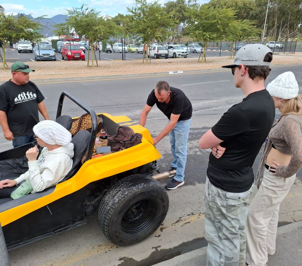 A yellow Beamish beach buggy is stranded on the roadside during Wiehann's Run, with club members inspecting it, indicating a breakdown and the need for a tow.