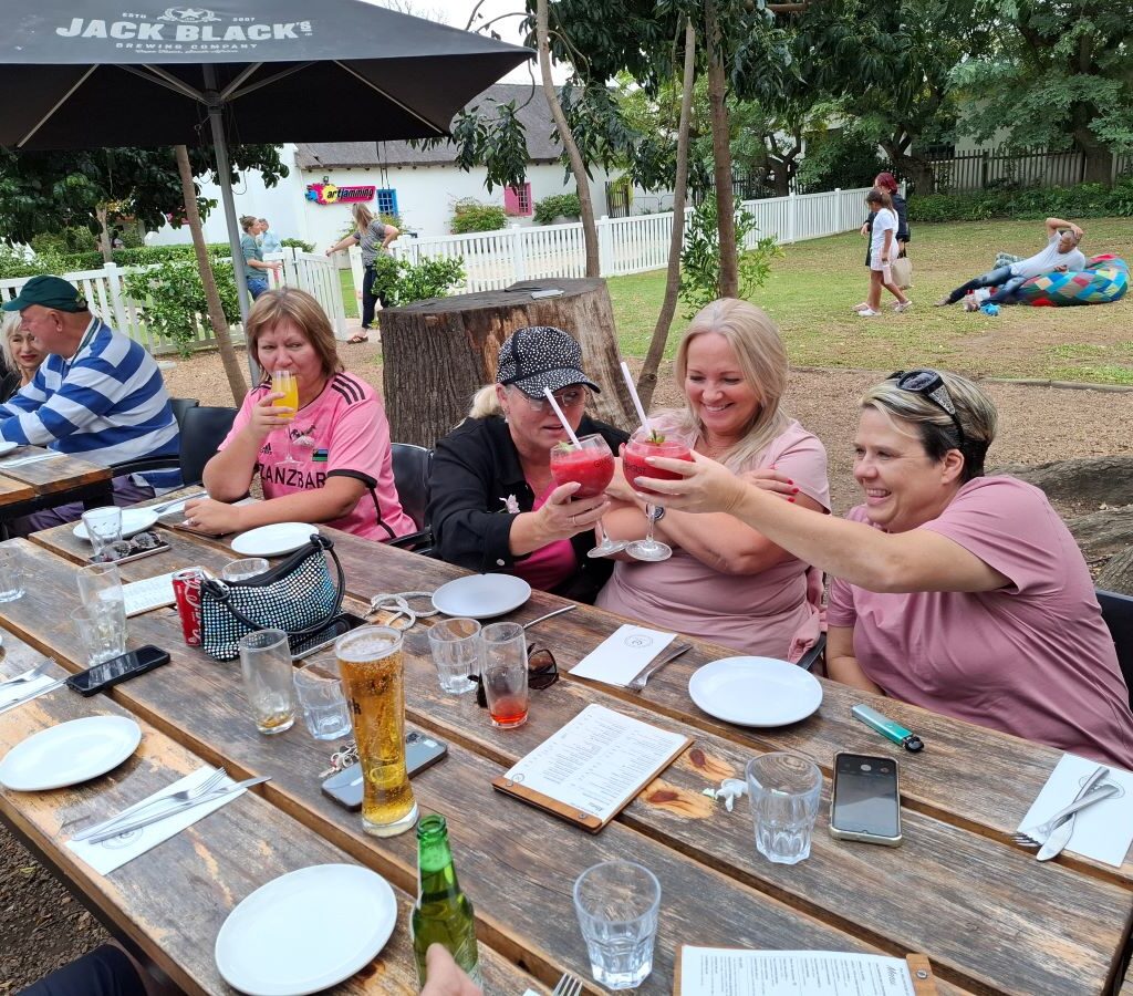 Wild Buggers Beach Buggy Club members, seated at a long table at Lourensford Estate, are raising glasses with cocktails, toasting and celebrating their successful Wiehann's Run.