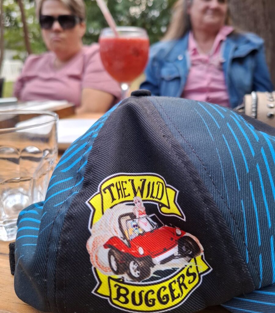 A vibrant image featuring the Wild Buggers Beach Buggy Club logo prominently, alongside a colourful cocktail, and two cheerful women, enjoying the relaxed atmosphere at Lourensford Estate during Wiehann's Run.