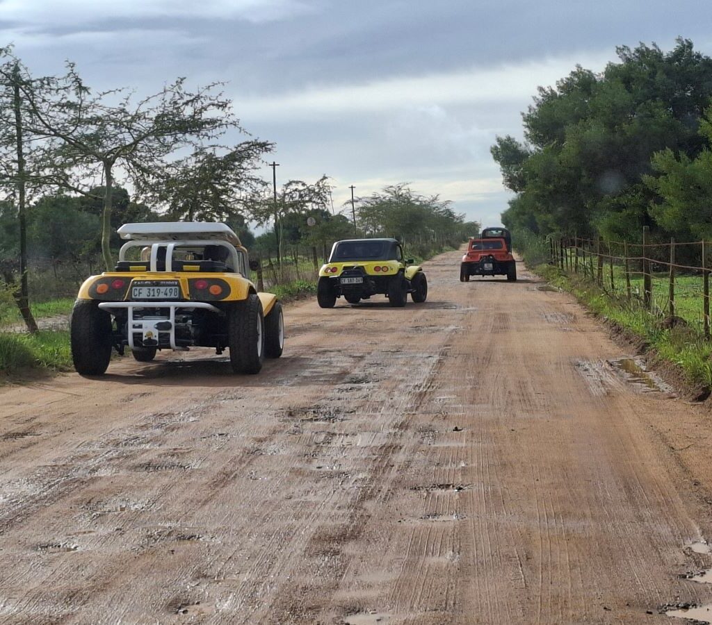 Chris, Anthony, Brent, and Tony driving their Beach Buggies and VW air-cooled vehicles down a wet gravel road towards the "African Savanna" during Tony & Sue's Adventure.
