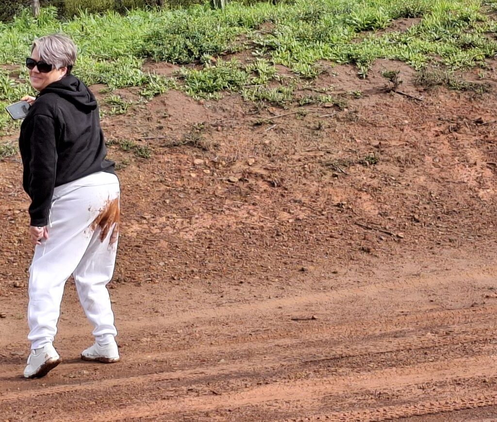Yolandie Ackerman standing on a wet gravel road after slipping and falling, with a noticeable wet mark on the back of her white pants, during The Wild Buggers' Tony & Sue's Run.