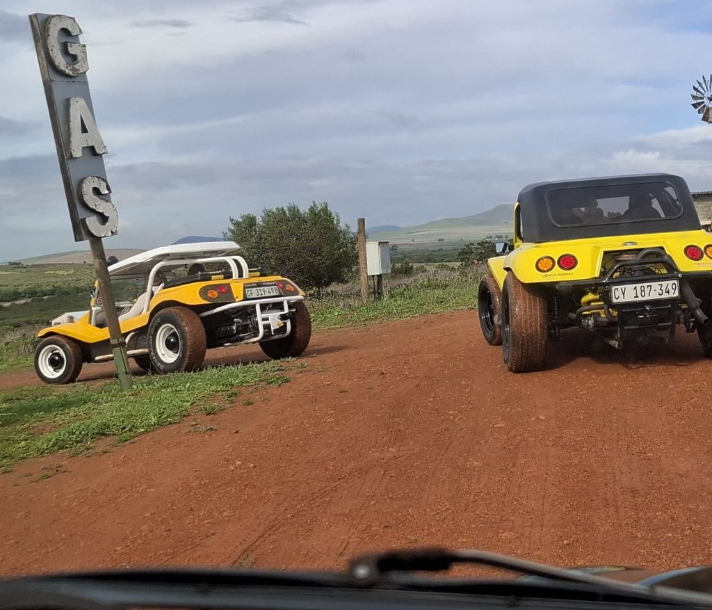 Two VW air-cooled Salamander Beach Buggies parked at the secret old-school gas station, near its vintage sign, during The Wild Buggers' Tony & Sue's Run.