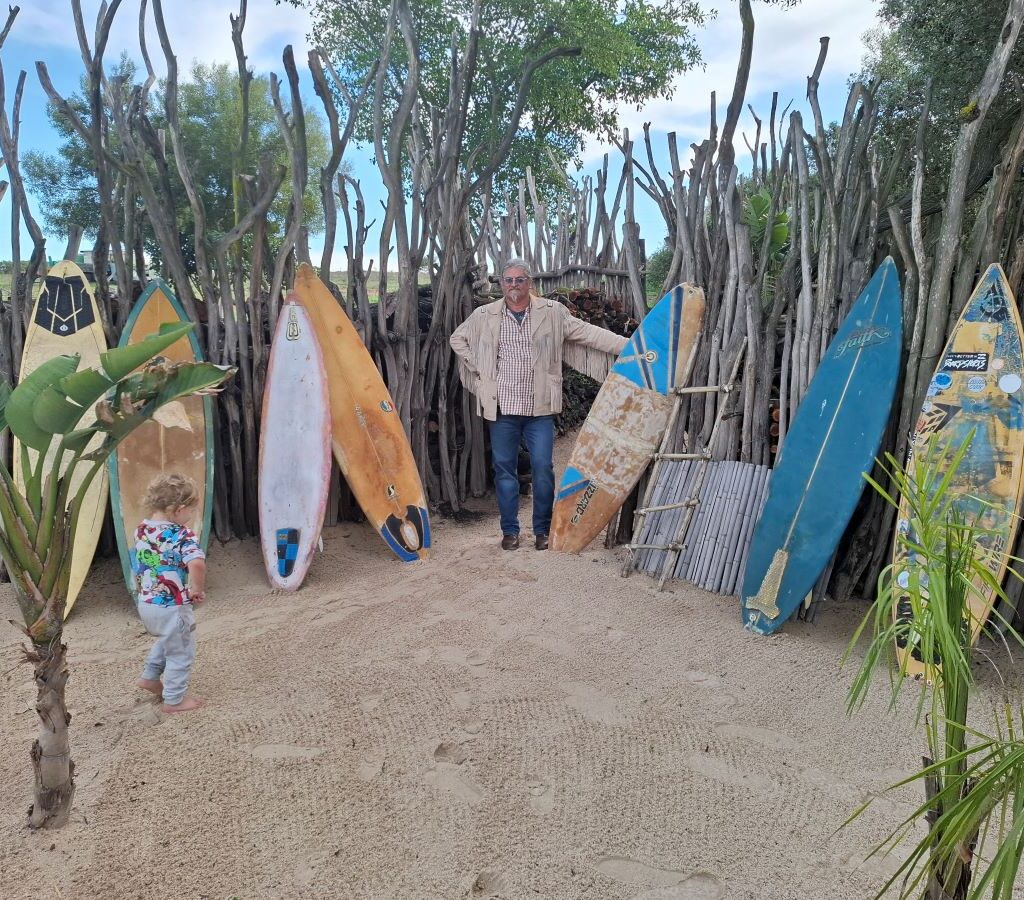 Tony Venter Sci Choo standing next to a display of surfboards at the "Mauritius" destination during The Wild Buggers' Tony & Sue's Run.