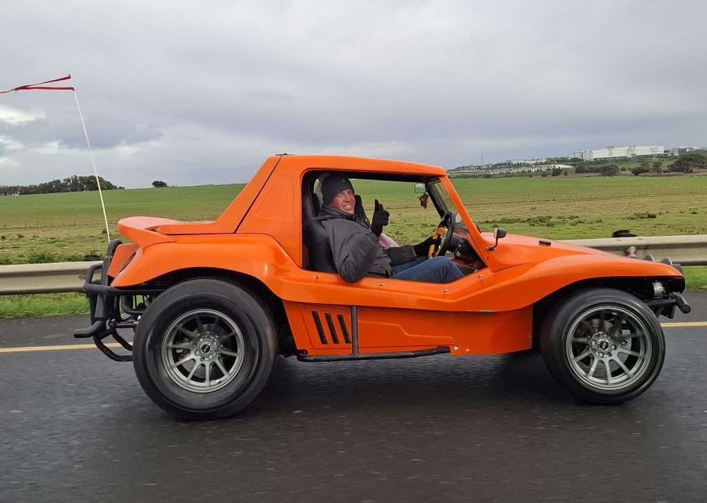 Anton and Mickey in their Baja Bug (unseen) on a road, taking a photo of Brent and Sam Van Der Weijde in their distinctive orange VW air-cooled Salamander Beach Buggy named The Wasp.