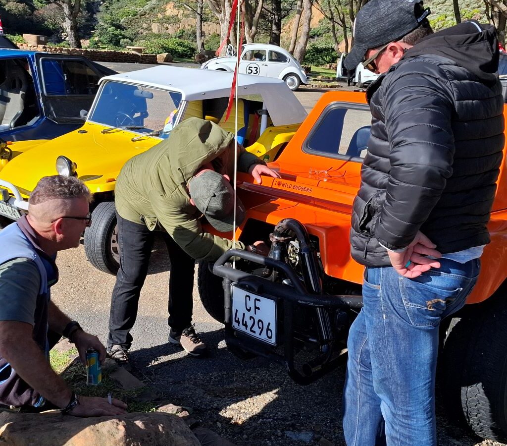 Brent & Sam's orange VW Salamander beach buggy 'The Wasp' with engine being inspected, focusing on carburetor issue