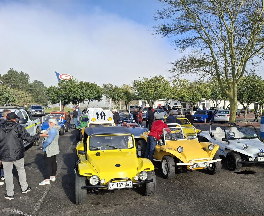A group of Wild Buggers Beach Buggy Club members and their classic VW vehicles, including Beach Buggies and VW Beetles, gathering at the meeting point on a sunny Sunday morning for Nick & Ellie's Run.