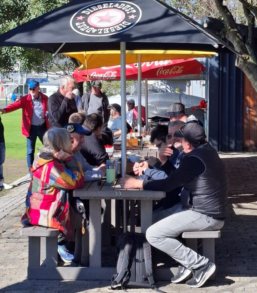 A photo of several Wild Buggers Beach Buggy Club members sitting together under the shade of trees, relaxing and drinking coffee during a break on Nick & Ellie's Run.