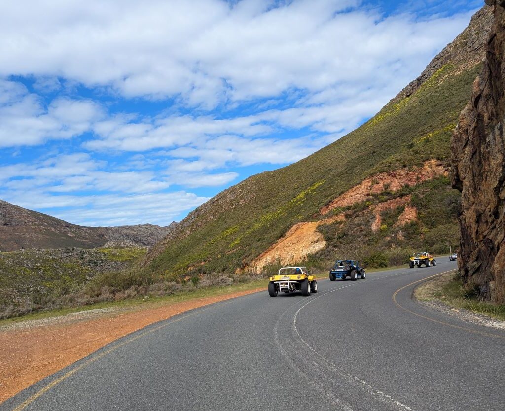 A photo of a convoy of Wild Buggers' beach buggies and VW Beetles continuing their drive on a winding mountain road on their way to Hellshoogte Pass.