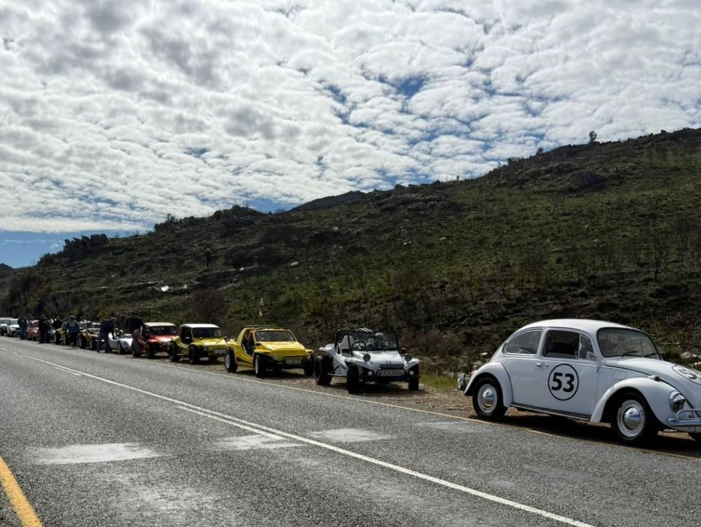 A photo of several Wild Buggers' beach buggies and VW Beetles parked on the side of a mountain road during a pitstop, with a stunning scenic view of the surrounding landscape.