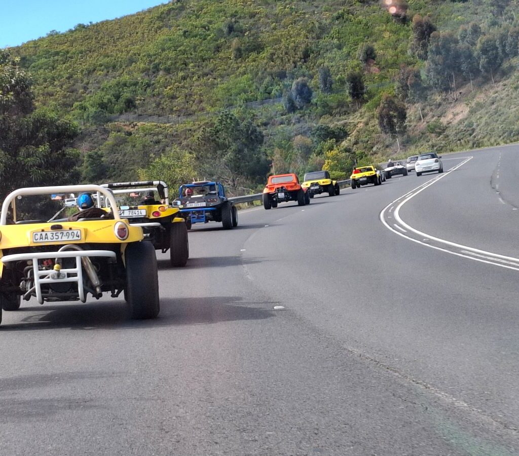 A photo of a convoy of Wild Buggers' beach buggies and VW Beetles driving on a winding mountain road, heading uphill.
