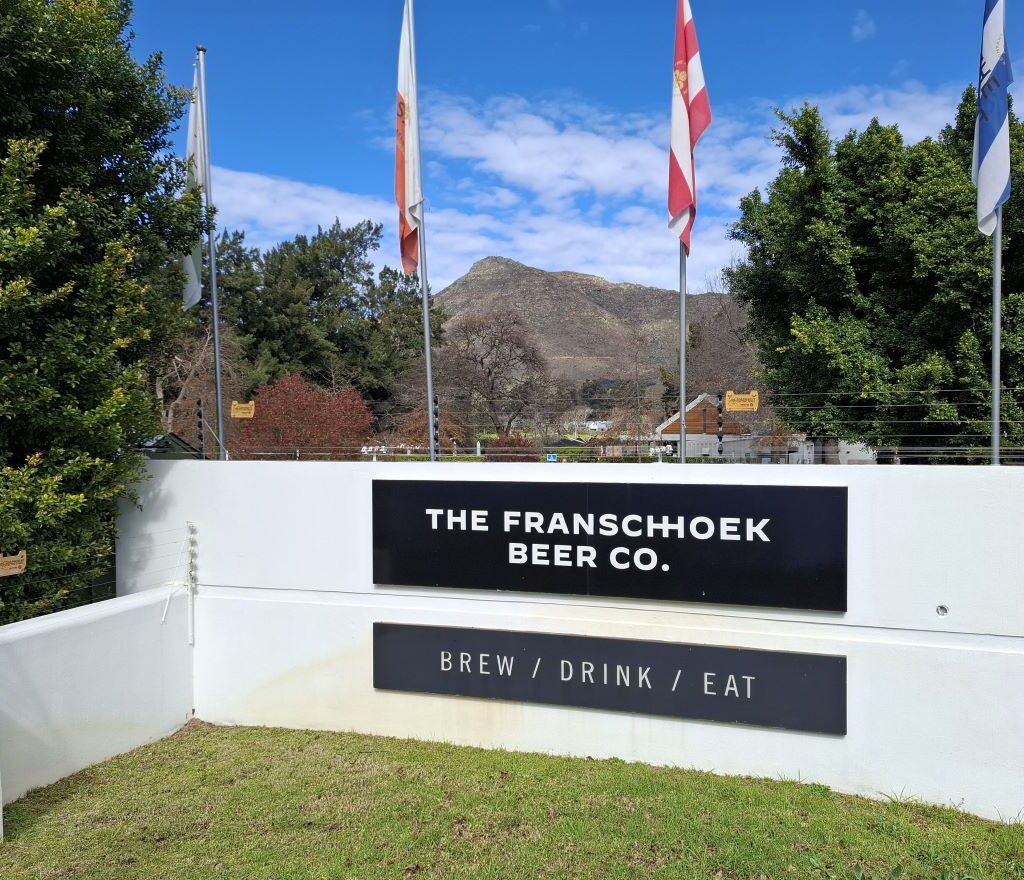 A photo of the entrance to the Franschhoek Beer Company, a brewery, with a sign that says "Welcome" and a path leading inside.