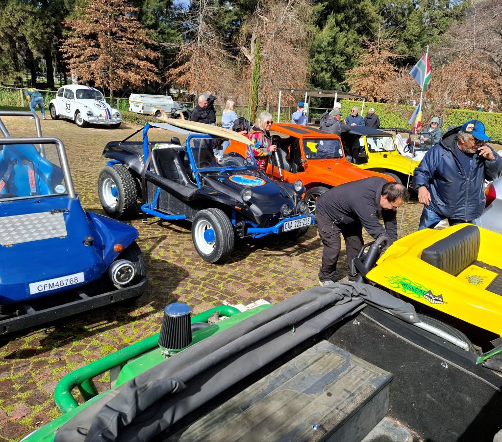A photo of several Wild Buggers' club members gathered around Fabian's Kango beach buggy in the parking lot of a brewery, looking to diagnose a problem with the vehicle.