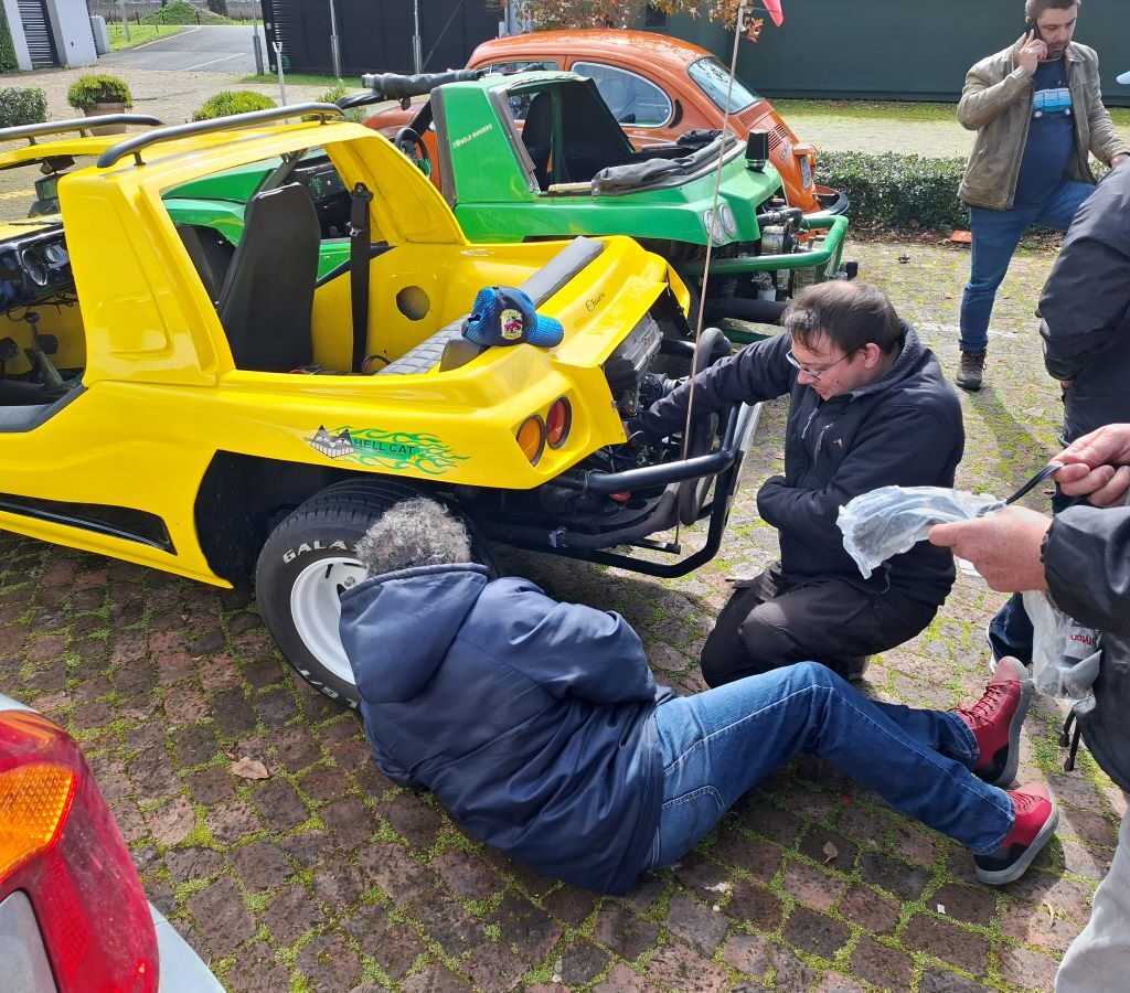 A photo of a group of Wild Buggers' club members gathered around Fabian's Kango beach buggy, using cable ties to fix a mechanical problem in the brewery parking lot.