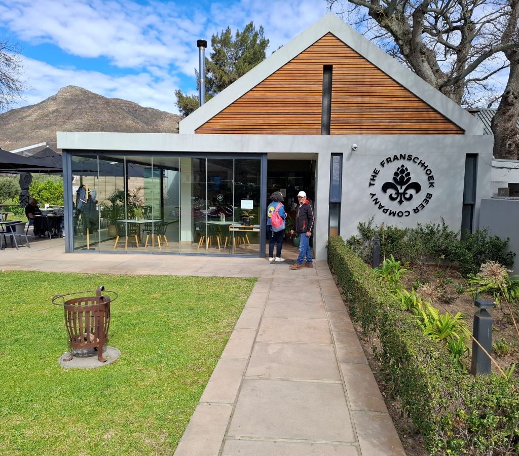 A photo of several Wild Buggers' club members walking through the entrance of the Franschhoek Beer Company, a large, modern-looking building with a welcoming interior.