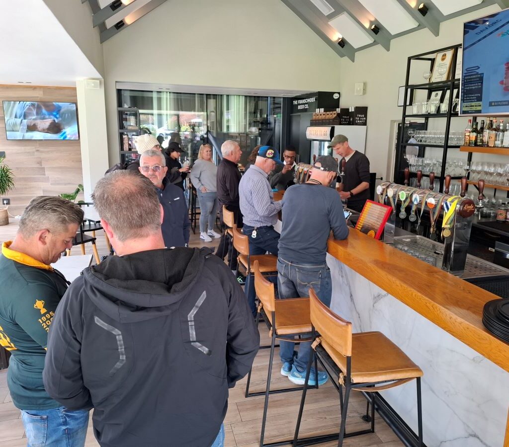 A photo of several Wild Buggers' club members standing at the bar inside the Franschhoek Beer Company, ordering beers after their drive.