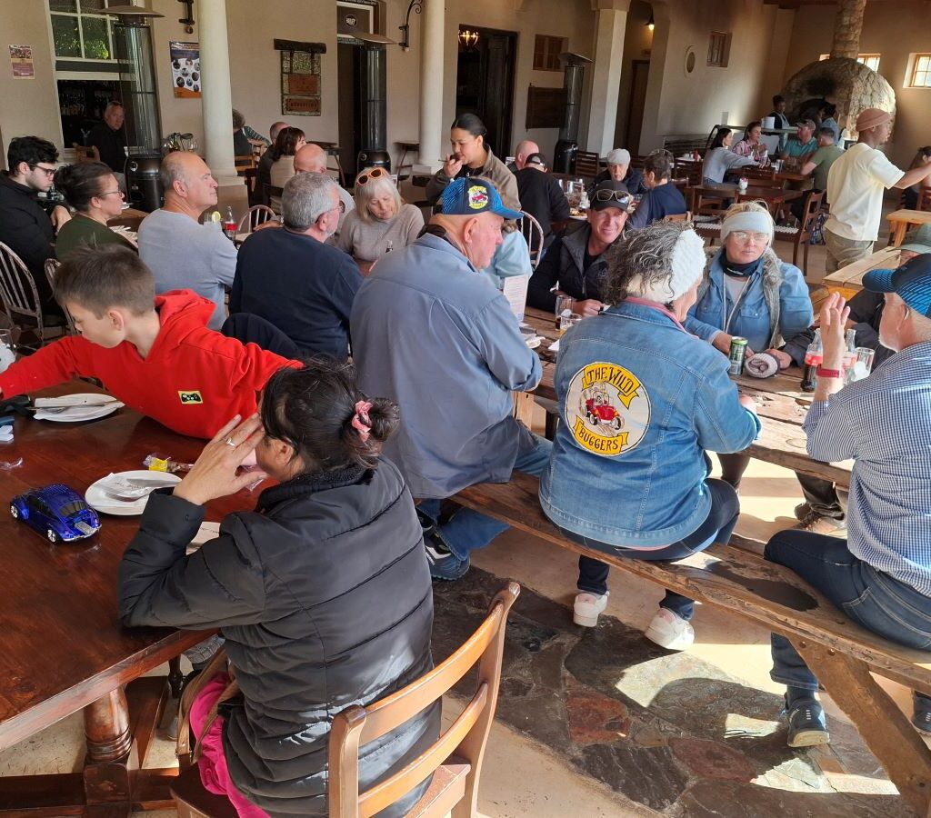 A photo of several Wild Buggers' club members sitting at a table at the Botrivier Hotel, chatting and relaxing together while waiting for the waiters to take their orders.
