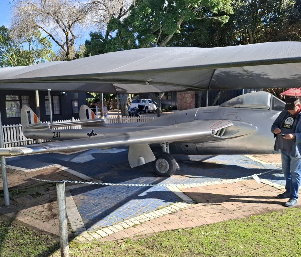 A photo of a vintage South African fighter plane on display at the Stellenbosch Flying Club, taken from a perspective that suggests Wild Buggers Beach Buggy Club members are viewing it during their coffee stop on Nick & Ellie's Run.