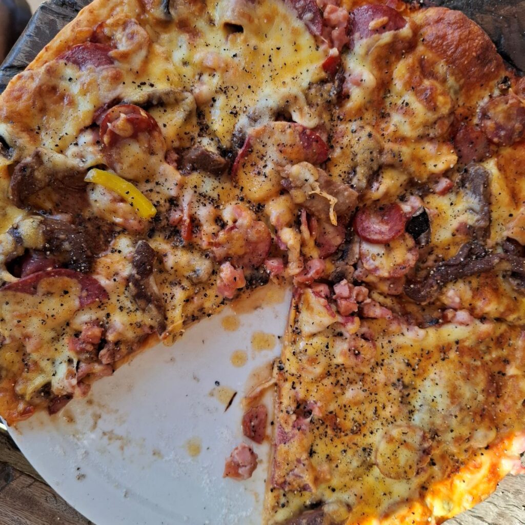 A close-up photo of a delicious-looking Carnivore pizza, loaded with meat toppings, served at the Botrivier Hotel.