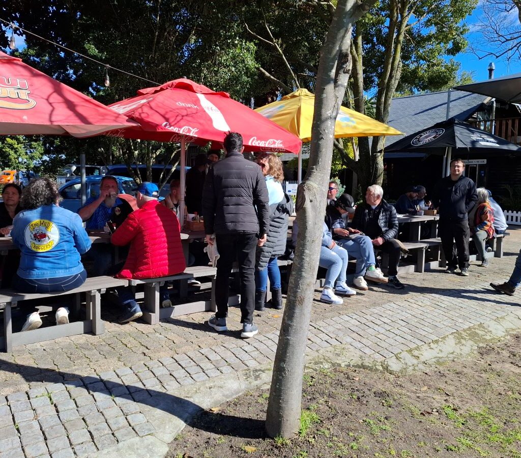 A photo of several Wild Buggers Beach Buggy Club members sitting on benches under the shade of trees, enjoying a break and waiting for their coffee during the Nick & Ellie's Run.