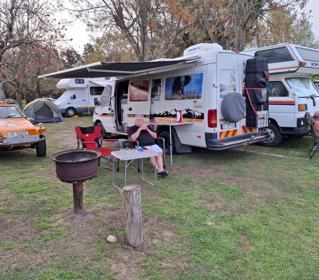 A photo showing three large Motorhomes parked and set up in a campsite, with the classic VW air-cooled vehicles and beach buggies of the owners—Nick, Clive, and Thys—parked nearby. The image captures the relaxed, ready-for-the-weekend vibe of the Wild Buggers arriving early for their club camp at Bergriver Resort.