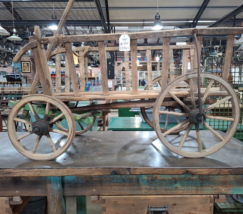 A charming photo of a beautifully detailed, handmade vintage wooden ox wagon model, displayed inside the Kooperasie Stories antique store during the Wild Buggers drive, showcasing a piece of classic South African history.