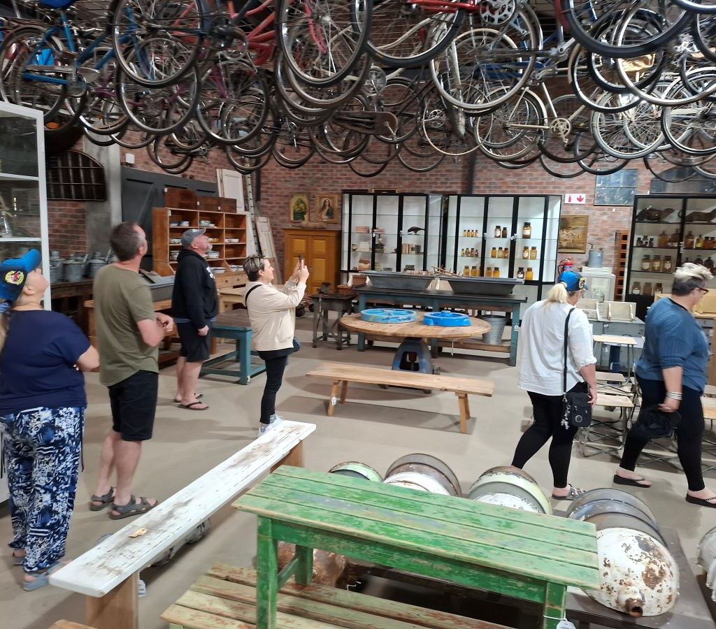 A candid photo inside the Kooperasie Stories antique store, showing members of the Wild Buggers Beach Buggy Club casually inspecting various unique vintage items and antiques during their drive pitstop in Simondium.