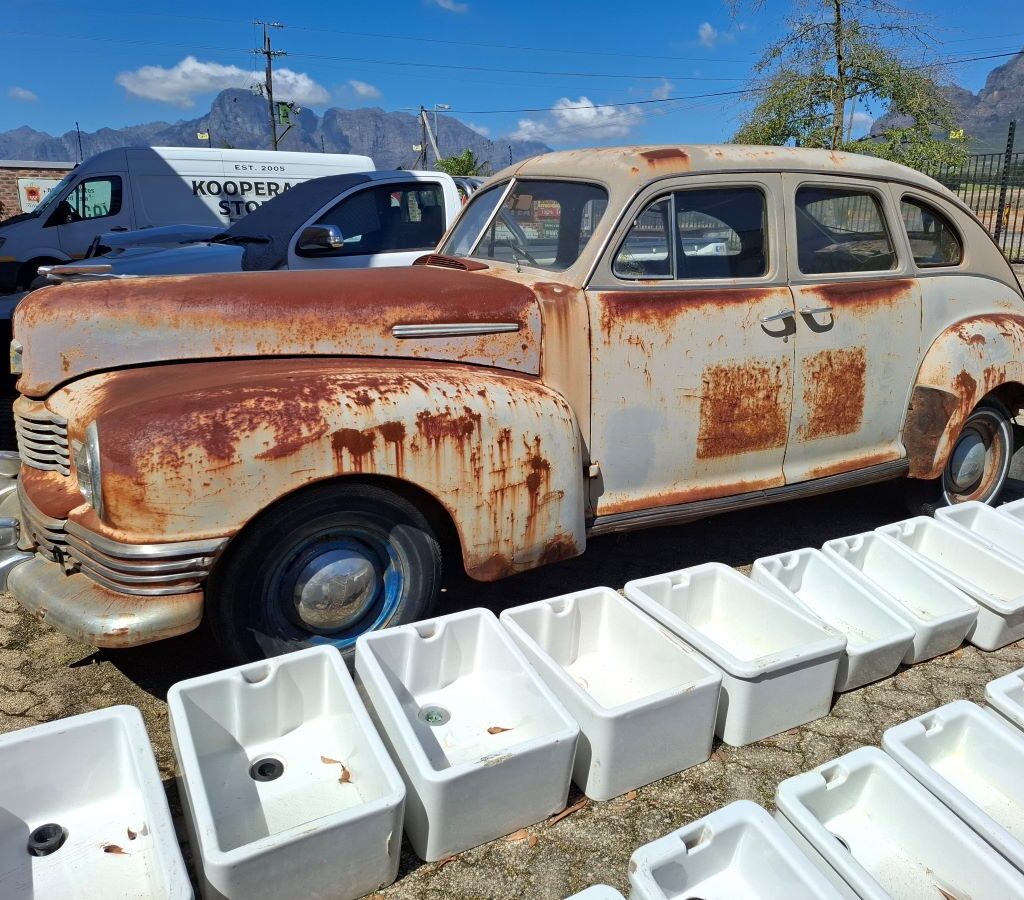 A photo of a very old, unidentifiable classic car with a vintage design, parked outside the Kooperasie Stories store, capturing a mysterious and interesting vehicle found during the Wild Buggers club drive.