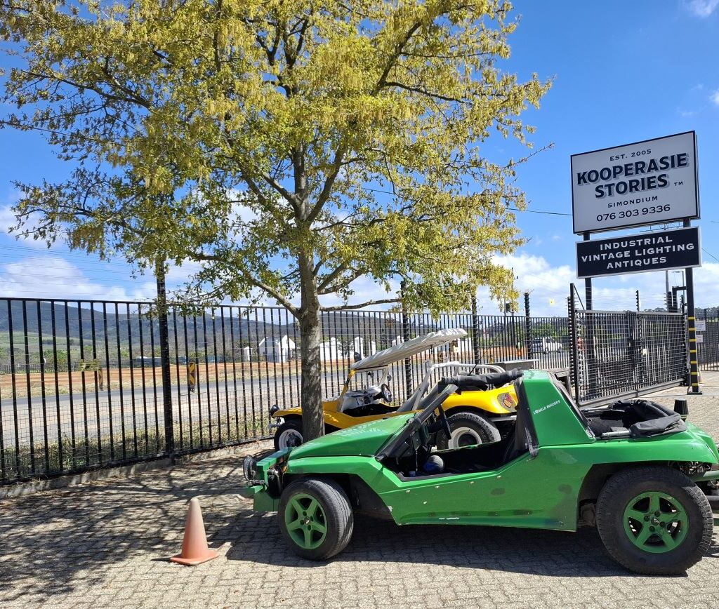 A dynamic photo of Anton’s green Kango beach buggy, Shrek, and Chris’s yellow Salamander beach buggy, Zara’s Buggy, parked side-by-side in the Kooperasie Stories parking lot as the drivers lock up, signaling the Wild Buggers are ready to continue their club drive.