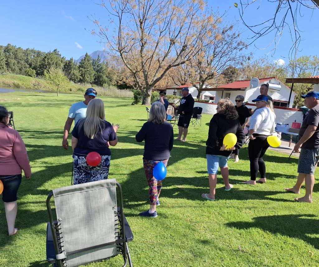 A hilarious action shot at the Bergriver Resort camp showing the six "Ladybugs" (Sandra, Sam, Michelle, Mickey, Yolande, and Linda) lined up, facing the men, with balloons tied behind their backs, signaling the start of a wild, impromptu game.