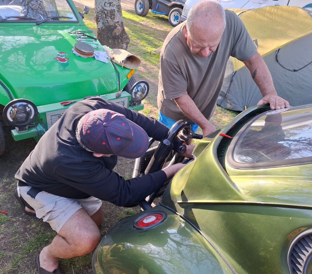 A candid photo taken at the Bergriver Resort camp showing club members Nick and Clive happily working on Mickey's green Baja Bug, Dark Side, in the campsite, solving its frustrating idling problem without being asked.