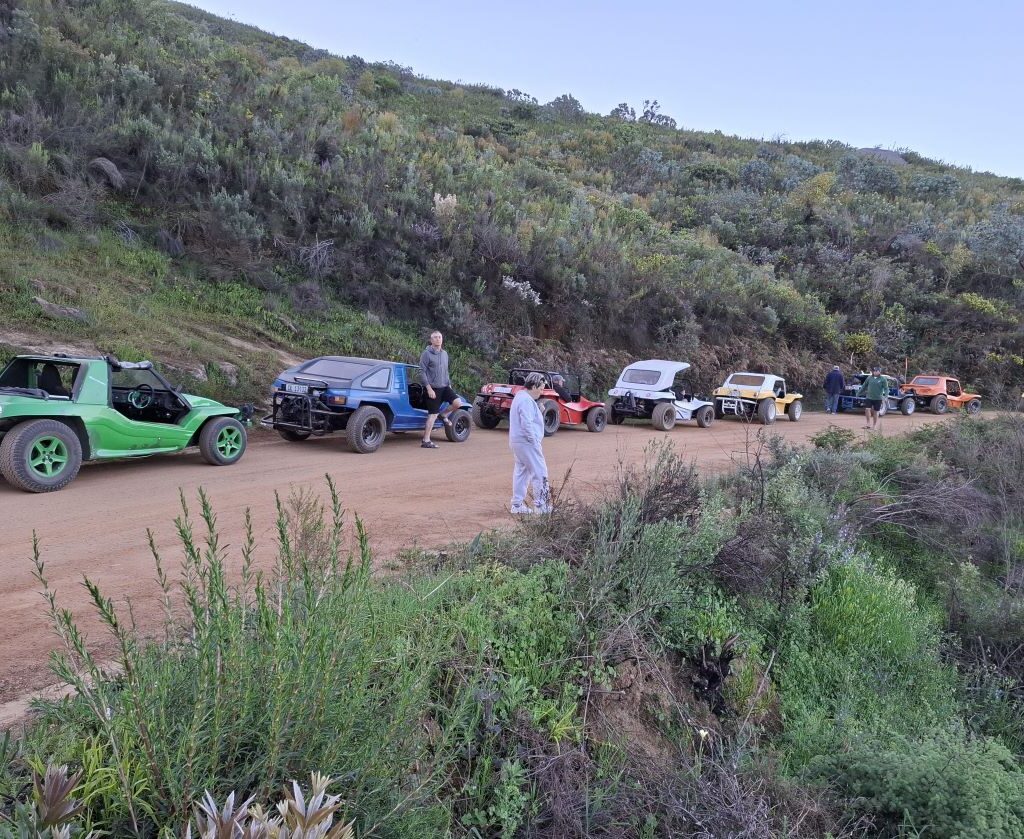 A beautiful and descriptive photo of several Wild Buggers members gathered near a small waterfall on the side of the road, having a relaxing chat after their scenic drive, capturing a moment of natural beauty and camaraderie.
