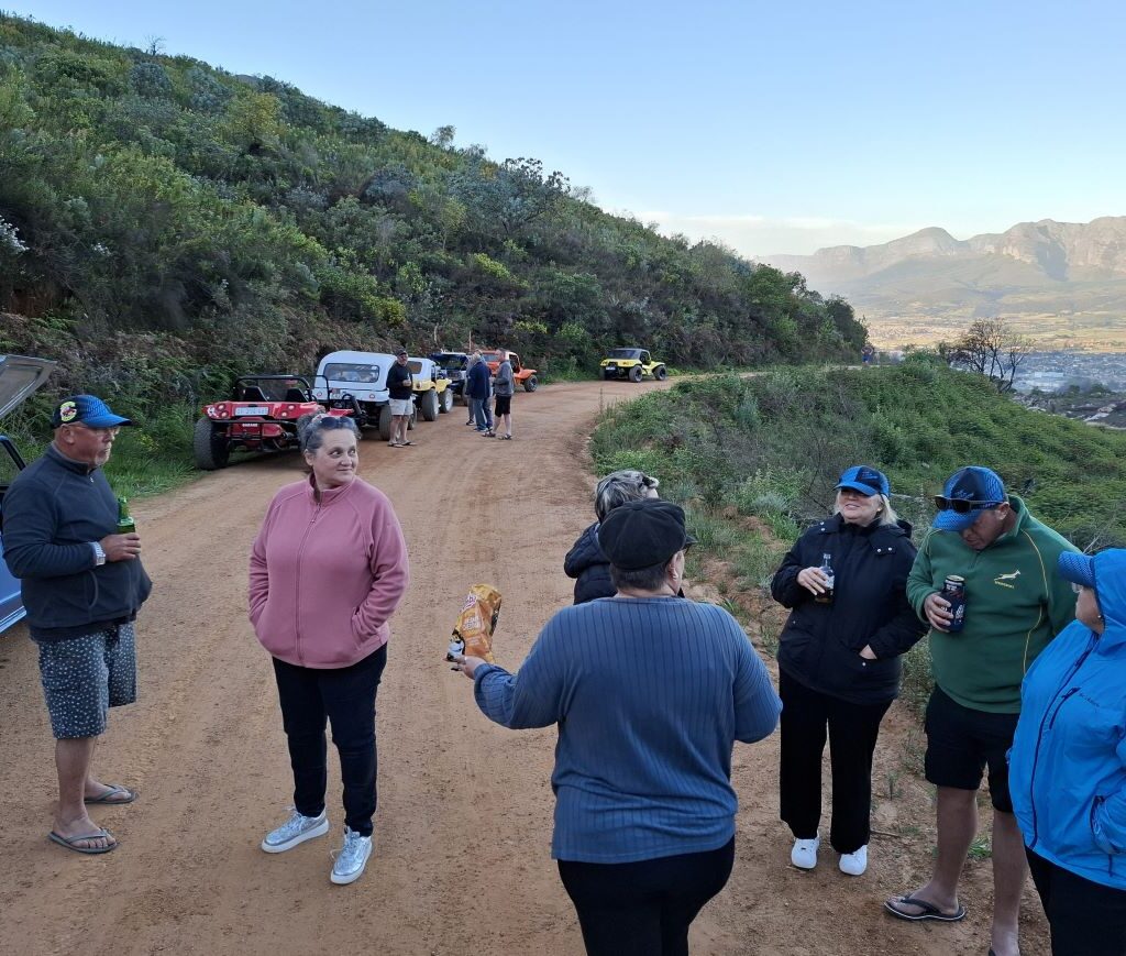A warm, candid photo of the Wild Buggers members gathered together on Paarlberg during sundowner, laughing, chatting, and enjoying the end of their epic drive, capturing the absolute jol (fun) of the VW Family.