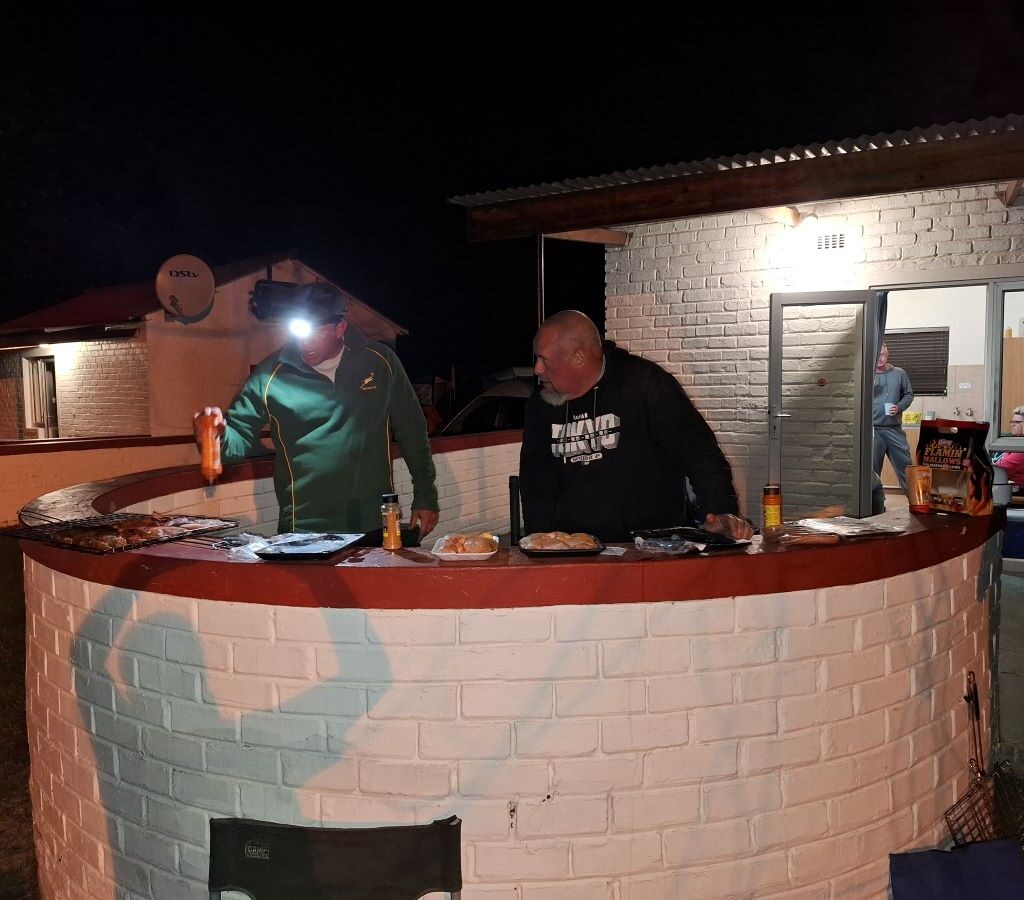 A candid and engaging photo of Wild Buggers members Brent Van Der Weijde and Anton Horne meticulously spicing the various cuts of meat (pork chops, steak, sosaties, lamb) that are packed onto a rooster (braai grid), preparing it for the evening braai at the Bergriver Resort camp.