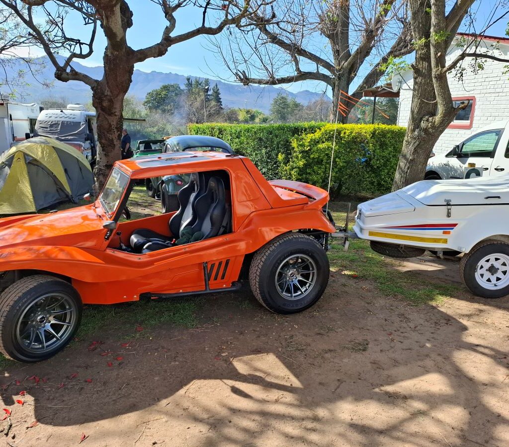 A photo taken at the Bergriver Resort camp showing Brent's orange beach buggy, The Wasp, hitched up to a small, packed trailer, highlighting the practical side of the VW air-cooled vehicles at the Wild Buggers event.