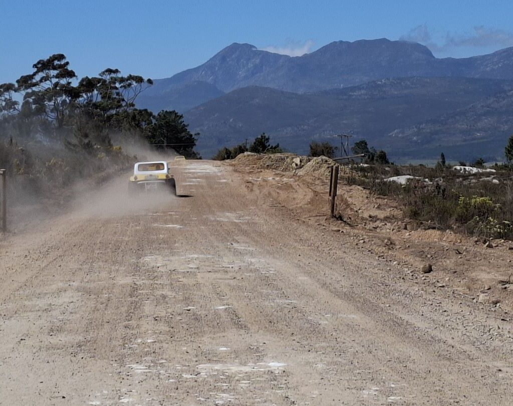 A line of Wild Buggers' VW Air cooled vehicles, including Beach Buggys, driving on the gravel Highlands Road.