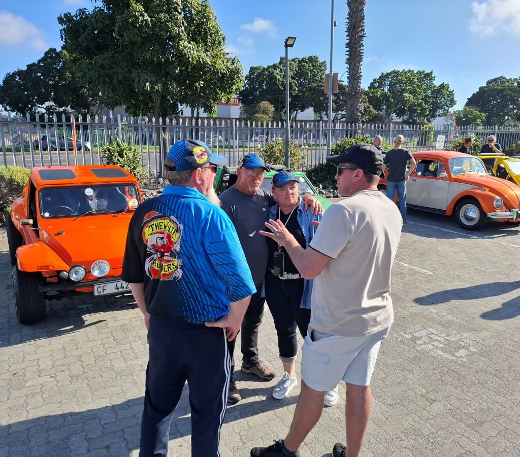 A group of Wild Buggers chatting and laughing at the meeting point with various air-cooled VW vehicles visible in the background.