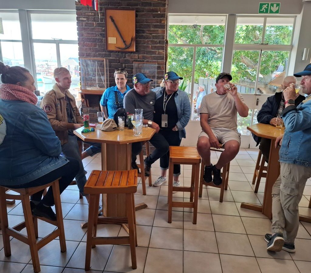 Several Wild Buggers club members are gathered inside the Gordon's Bay Yacht Club, standing and sitting and chatting.